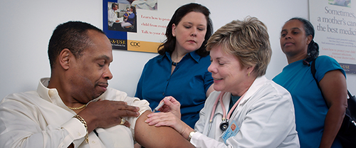 A nurse giving a shot with 2 people looking over it