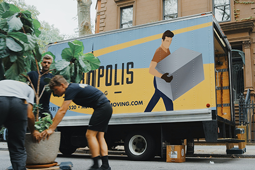 Three men picking up a large tropical plant to put in a moving truck parked on a New York street